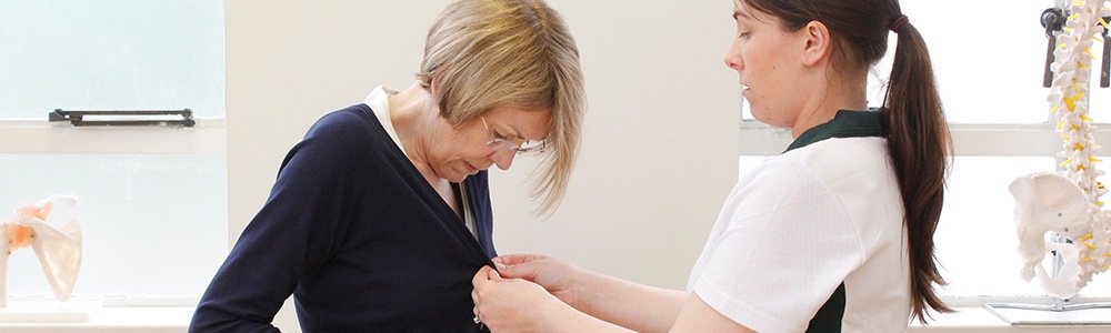 Liverpool OT therapist aids patient in buttoning a cardigan during therapy.